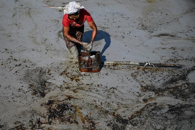 A woman salvages spilled oil from a pond filled with mud and filth. (AFP)