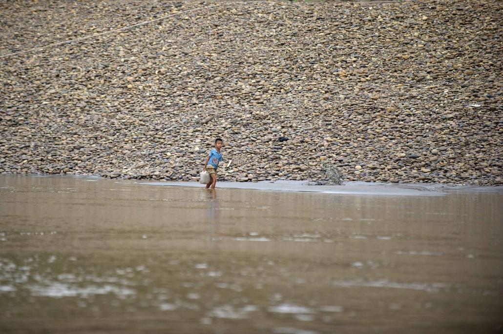 A boy carries a water bucket while walking through the shallows of the Thanlwin River in Kayah State. (AFP)