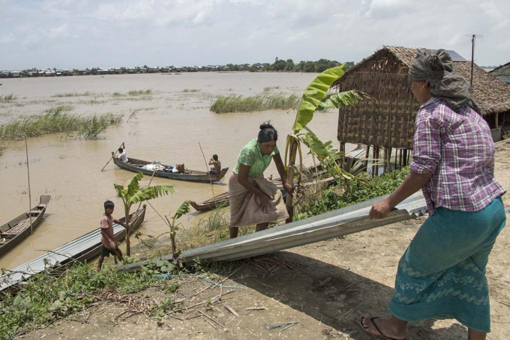 Ngapyaw Taw residents unload sheets of corrugated iron from a small boat onto the dyke, where they are rebuilding their homes. (Nyein Su Wai Kyaw Soe | Frontier)