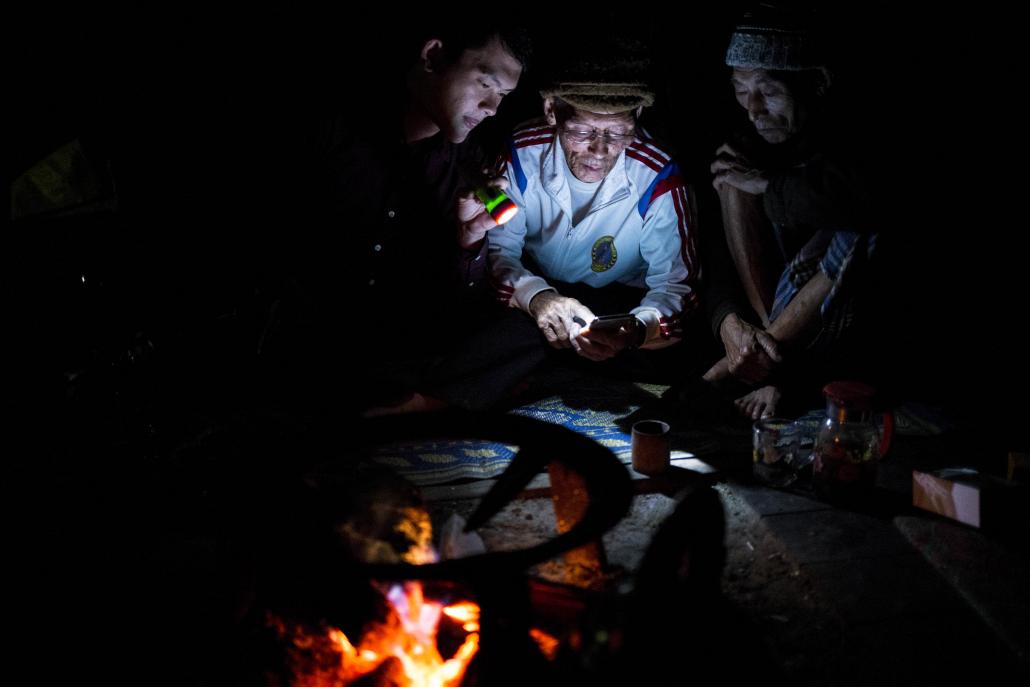 Residents of Zino village in Putao Township, Kachin State, use a cellphone in their living room. There is no electricity or cellphone connection in the village, but residents are confident the situation will soon change. (Ann Wang / Frontier)