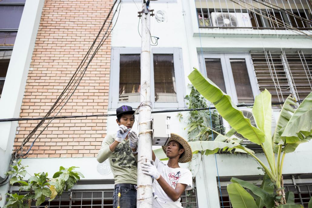 Two electrical workers conducting maintenance on a power pole in Yangon. (Ann Wang / Frontier)
