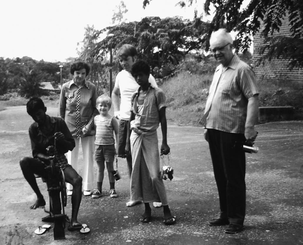 Harry Huskey, right, and Sheldon Bachus, rear, watch on as a man sharpens a knife outside their residence in Yangon. Both Huskey and Bachus worked at University of California at Santa Cruz and were sent to Burma under the UCC project. (Supplied)