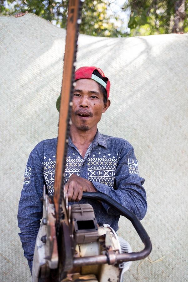 A villager from Mahu poses with his chainsaw in front of one other source of meagre local income: a mat made of dry bamboo. (Ann Wang | Mongabay)