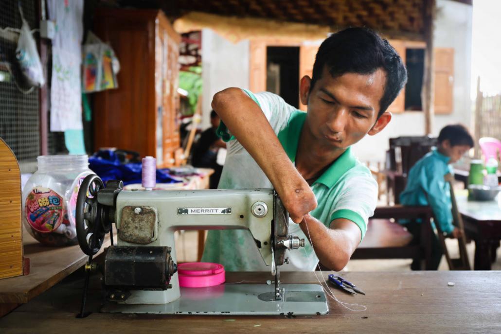 လက်ဖဝါးနှင့် လက်ချောင်းများမပါဘဲ မွေးဖွားလာသည့် ကိုဆန်းထူးက ဈေးကွက်တင်ရောင်းရန် အဝတ်အထည်များ ချုပ်လုပ်ရန်ပြင်ဆင်နေစဉ်။ ဓာတ်ပုံ - ဗစ်တိုးရီးယား မီလ်ကို