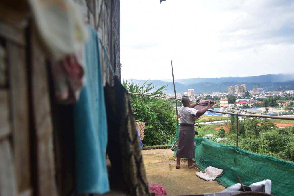 U Than, a migrant from Sagaing Region, hangs out a longyi to dry at his house in Muse's Christian ward, with the modern buildings of the Chinese city of Ruili visible in the background. (Kyaw Lin Htoon | Frontier)