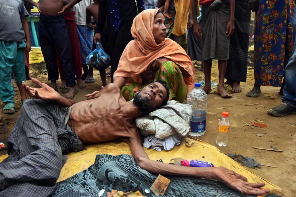 Sayed Agbar lies on the side of the road in the arms of his wife south of Cox's Bazar, shortly after making a hazardous crossing from Rakhine State. (Steve Tickner | Frontier)