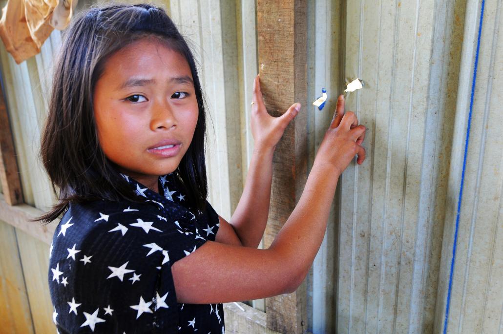 Kachin teenager Bawk Nu Mai shows where shrapnel tore through the wall of a washroom near her home in the Maung Lai Hkyet IDP camp north of Laiza. The camp was shelled by the Tatmadaw on December 18. (Steve Tickner | Frontier)