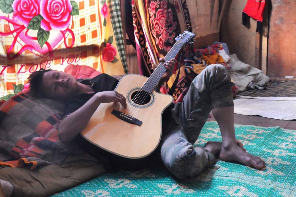 A young Kachin man plays guitar inside his family's shelter at Woi Chyai. (Steve Tickner / Frontier)