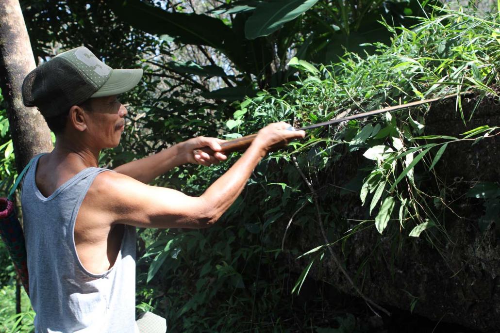 A Wae Ka Wah resident clears vegetation from around a Japanese bunker in a rubber plantation behind the village. (Thomas Kean | Frontier)