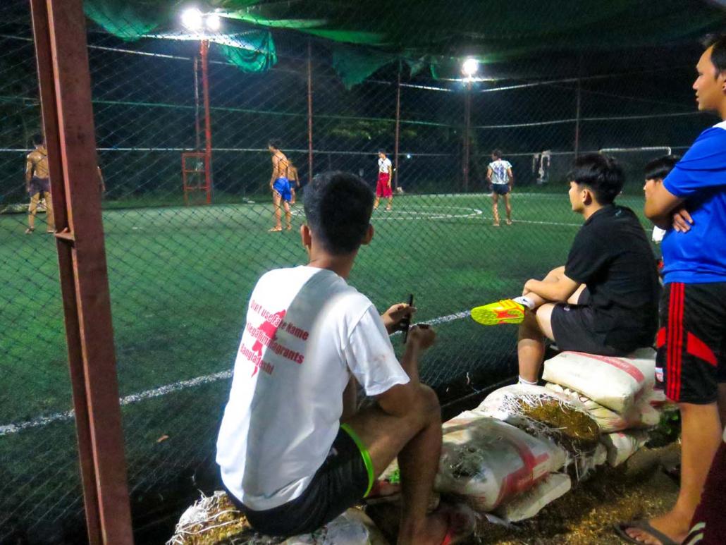 Young men wait for their turn to play futsal, and shout encouragement at players, at a court in South Dagon. (Kyaw Lin Htoon | Frontier)