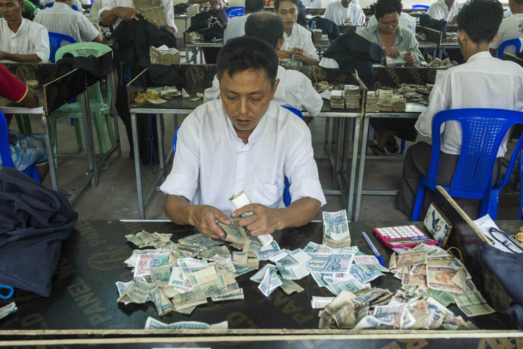 An employee works through piles of small change at the YRTA office in Yangon. (Teza Hlaing | Frontier)