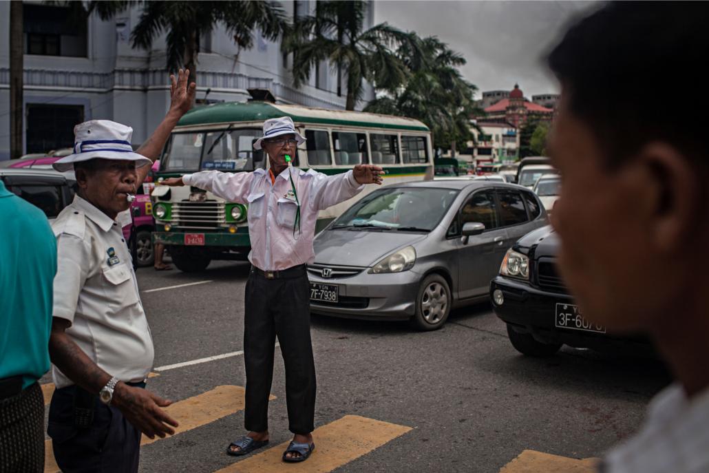 Officer Tun Tun Aung, centre, and his colleague direct traffic on Sule Pagoda Road during rush hour in downtown Yangon. (Lauren DeCicca / Frontier)