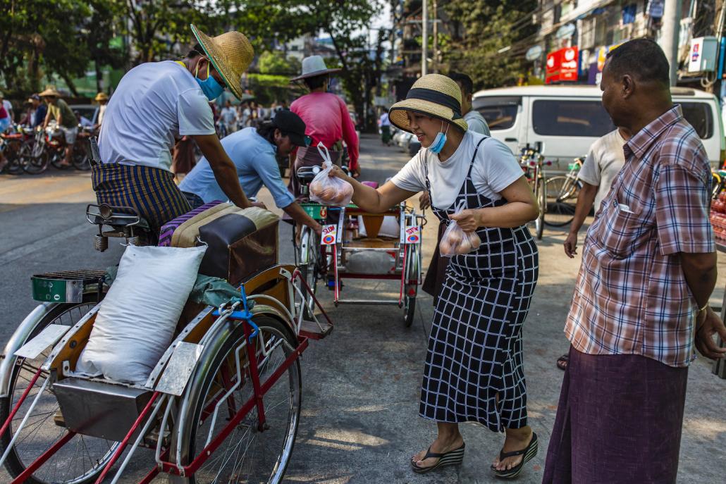 A volunteer hands eggs donated by a restaurant to trishaw drivers at a food distribution event in Sanchaung Township on April 9. (Hkun Lat | Frontier)