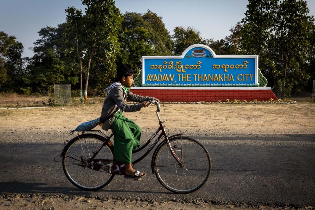 A cyclist rides past a sign welcoming visitors to "Thanaka City" in Ayadaw Township. (Hkun Lat I Frontier)