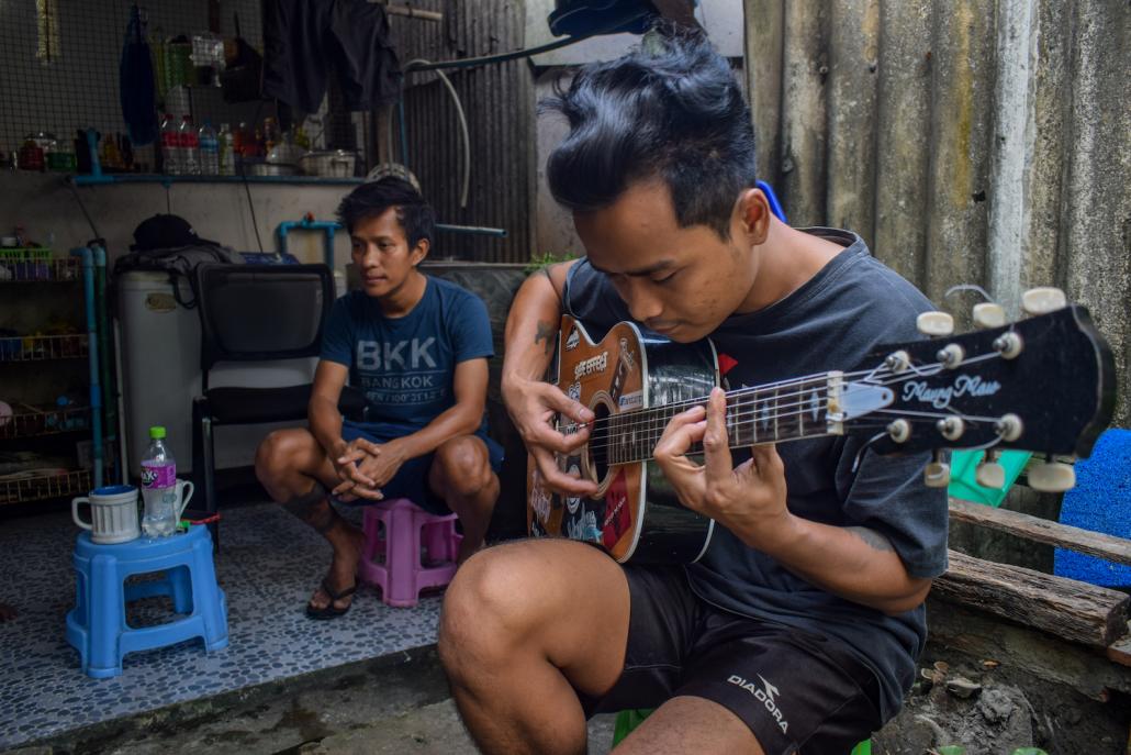 Ko Htay Lin (rear) sits with a colleague as he plays the guitar. Both work for an informal crew that services air conditioners, but a lack of work has left them without any income. (Kyaw Lin Htoon | Frontier)