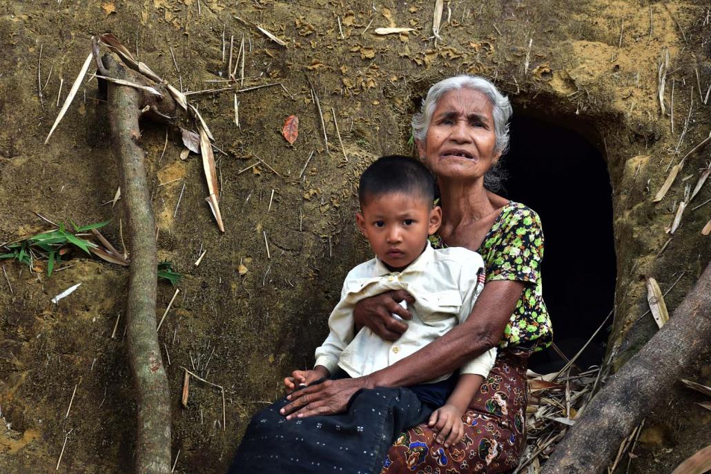 Rakhine grandmother Daw Aye Thein Nyo, 68, with her grandson, Mg Naing Lon Soe, 4, at the entrance to a bomb shelter dug into a hill behind their house in Myoma Zayti Taung village, Buthidaung Township. (Steve Tickner | Frontier)