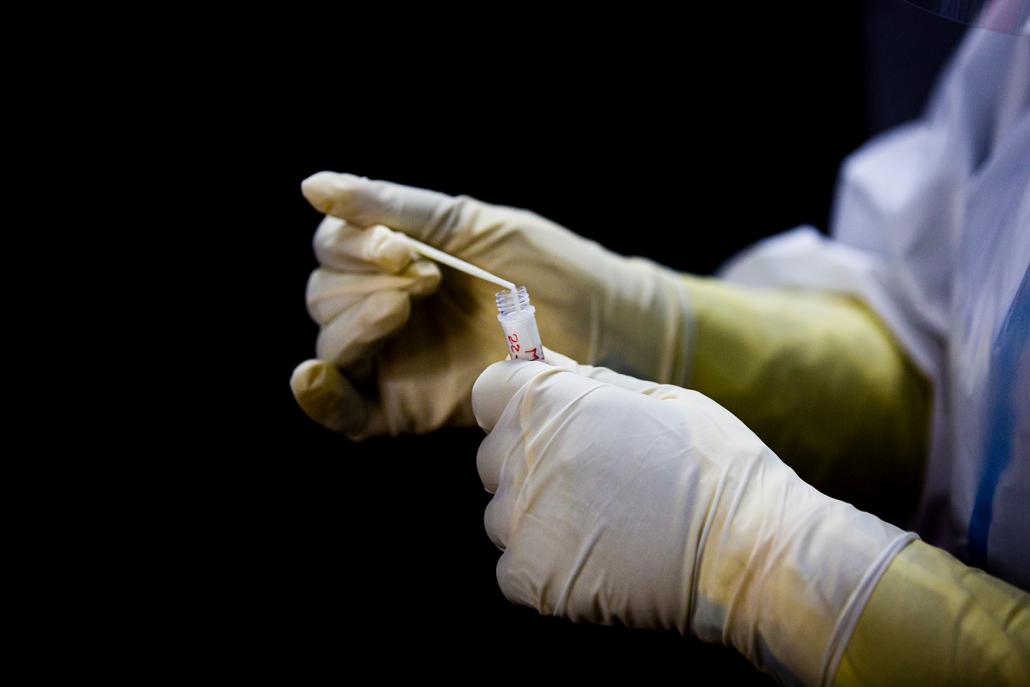 A medical worker places a sample into a viral transport medium tube on May 22. The workers who collect samples every day are at the most risk of exposure to the virus. (Hkun Lat | Frontier)