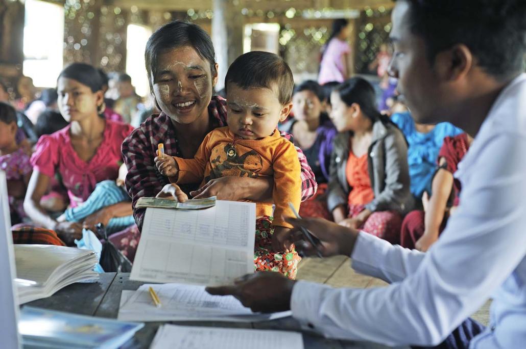 A mother collects her maternal and child cash transfer payment from Tat Lan staff in Yoe Sa Nwin village during a mother-to-mother support group meeting. (Kaung Htet | Tat Lan)