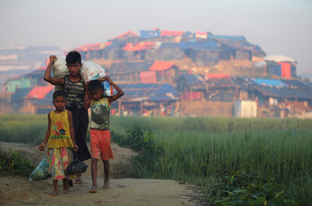 Rohingya children carry sacks of donated food outside of a Rohingya refugee camp in Bangladesh. (AFP)