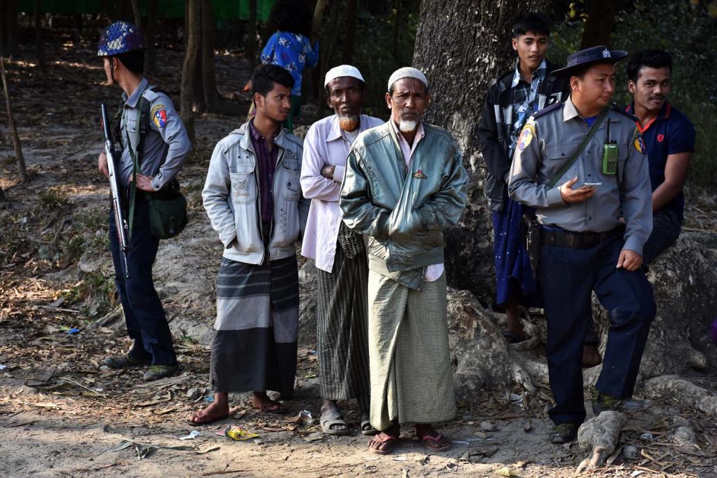 A group of Rohingya men stand beside police officers in Nyaung Chaung village near Maungdaw town. (Steve Tickner | Frontier)