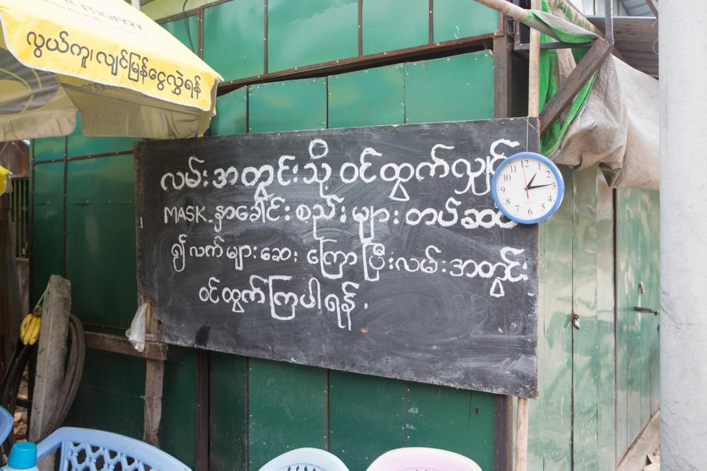 A signboard warns people to wear facemasks and wash their hands before entering the street. (Thuya Zaw | Frontier)