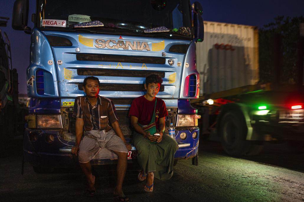 Truck driver U Kyaw Zeya (left) sits on the front of his vehicle near Botahtaung jetty on April 24. Since the introduction of a nighttime curfew on April 18, drivers have switched to working in the daytime. (Hkun Lat | Frontier)