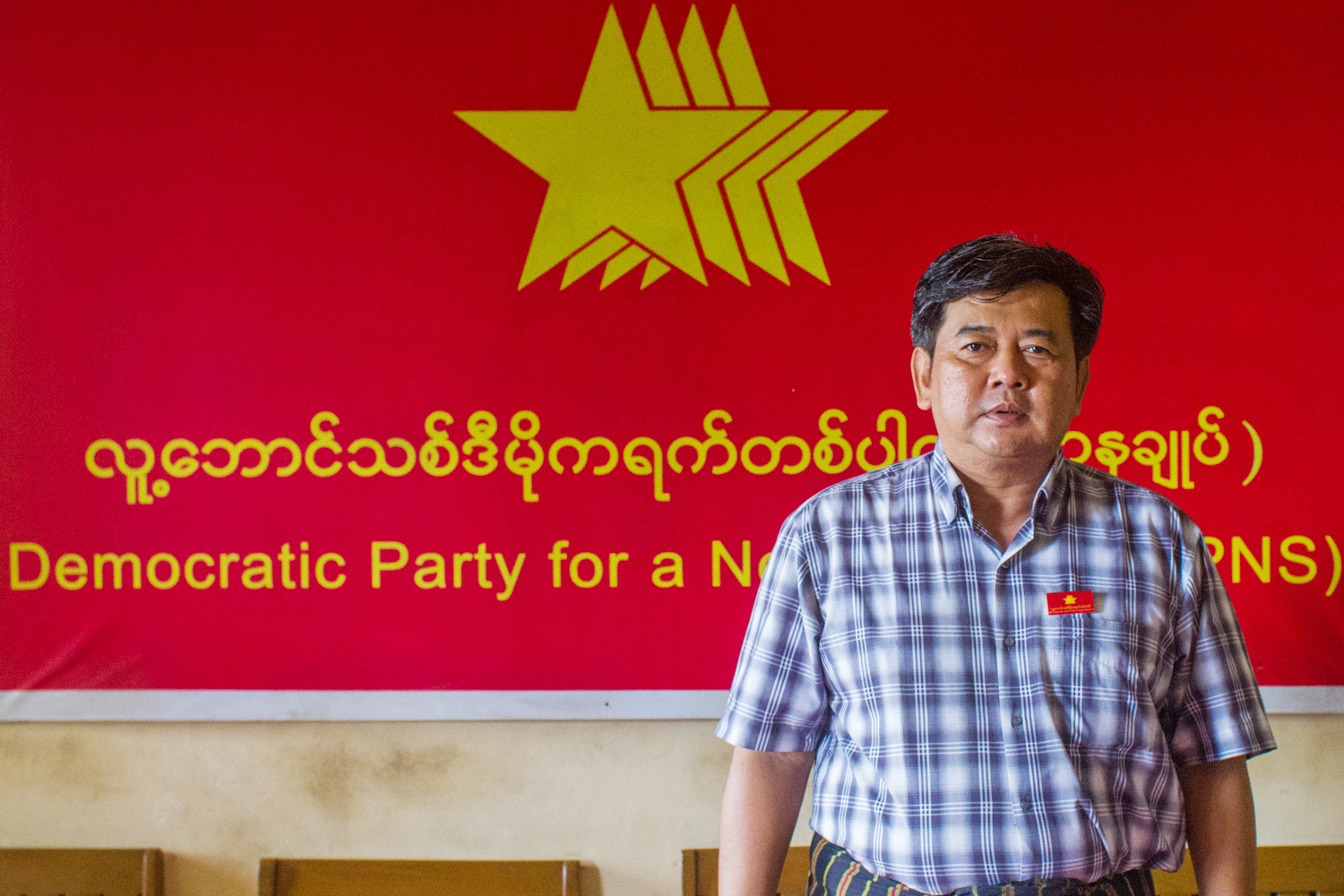 Longtime democracy activist and chair of the Democratic Party for a New Society U Aung Moe Zaw stands before a party signboard. (Mar Naw | Frontier)