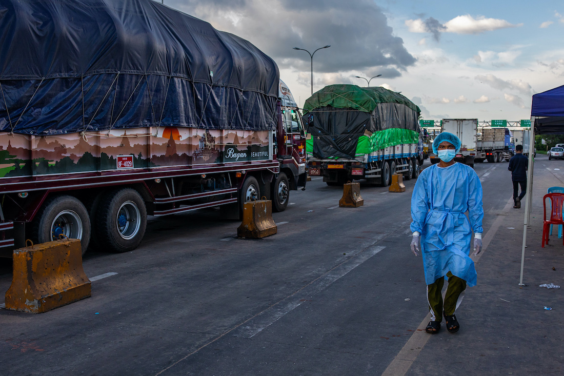 A medical worker walks past trucks lined up at a toll gate along the Yangon-Mandalay Highway, their drivers waiting to be tested for COVID-19. Travel restrictions and COVID-19 transport protocols have caused major disruptions to the country's logistics network. (Hkun Lat | Frontier)