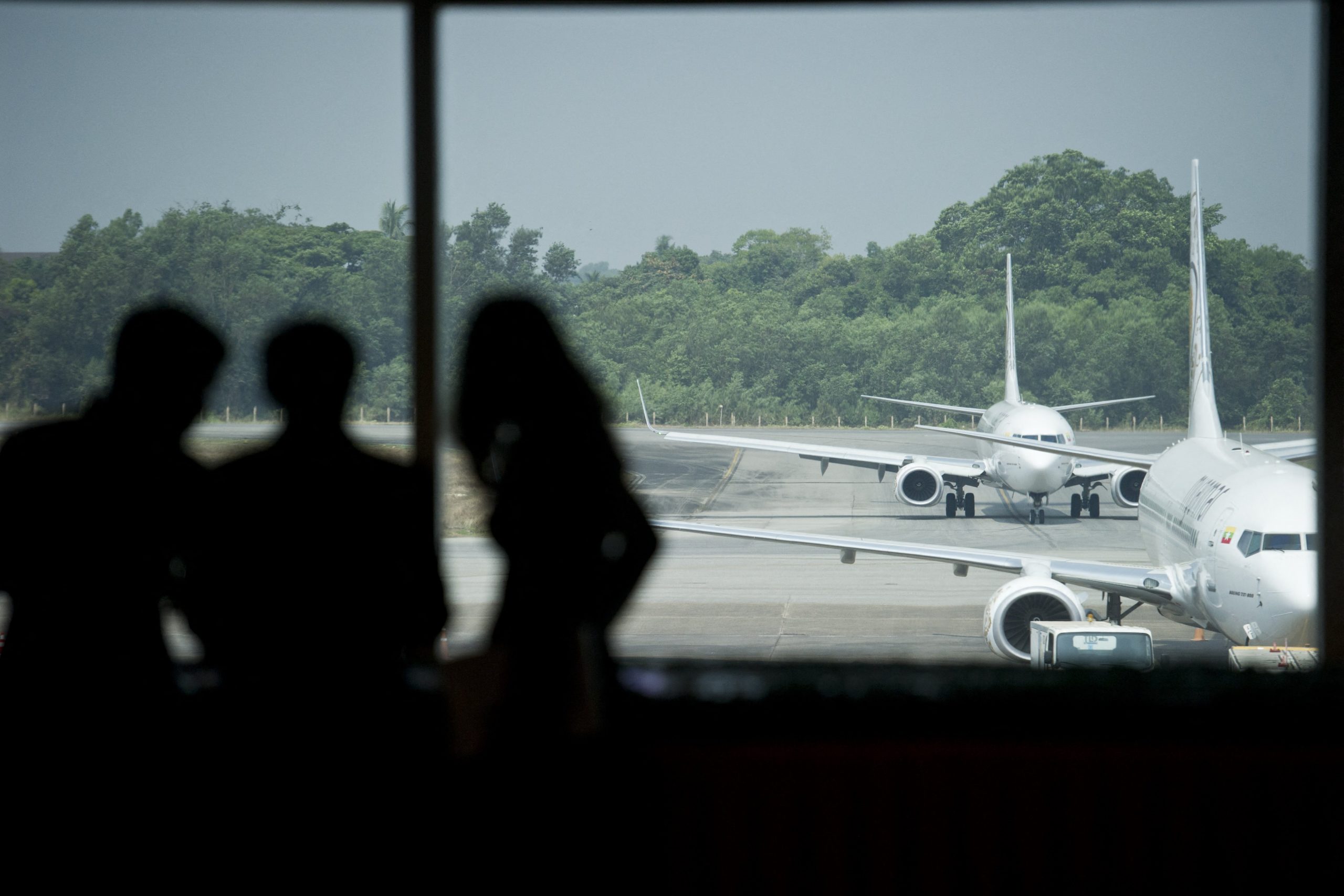 People look on as aircraft are seen from the window of a terminal at Yangon International Airport. (AFP)