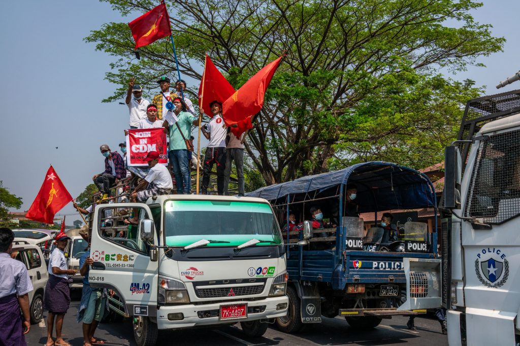 Protesters wave NLD flags and shout slogans beside a police truck during a protest against the military coup in Yangon on February 22. (Frontier)