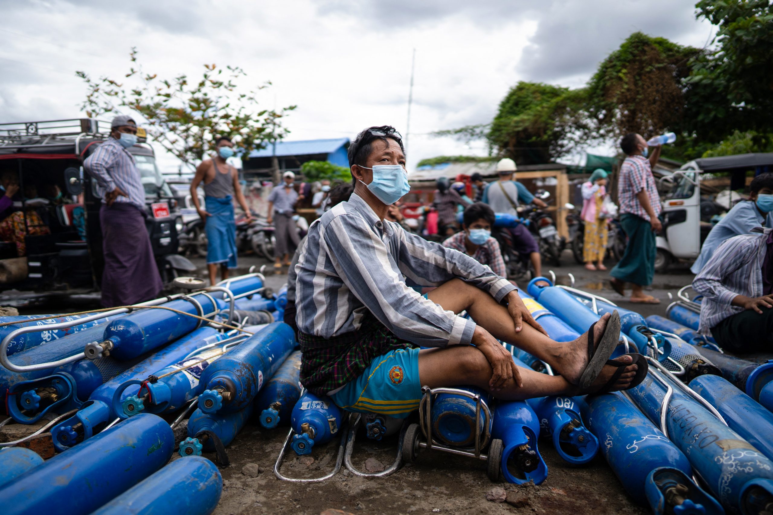 A man sitting on empty oxygen canisters outside a factory in Mandalay on July 13, 2021 (AFP)