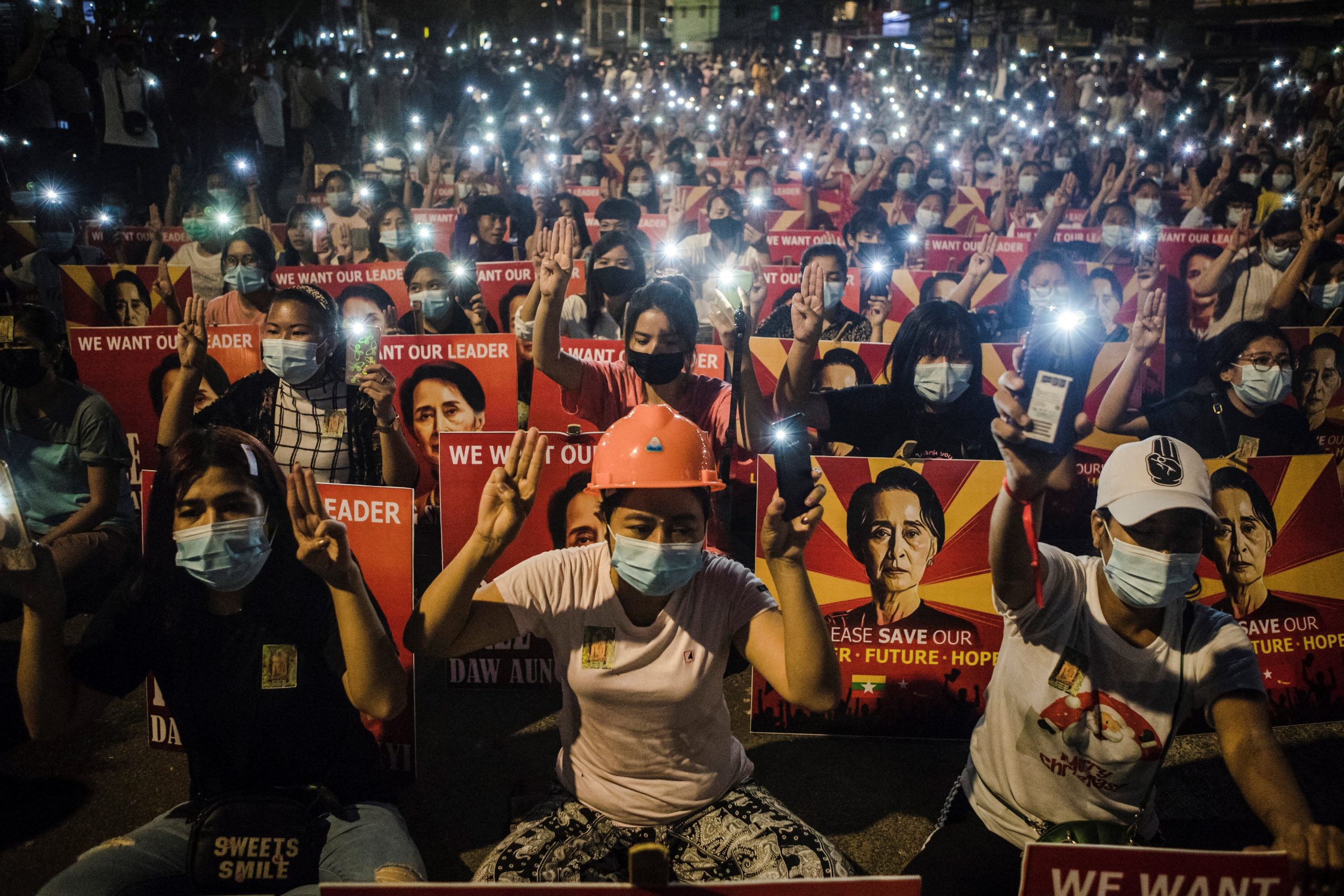 Taken on March 12, 2021, protesters hold up the three finger salute and placards with the image of Aung San Suu Kyi while using their mobile torches during a demonstration against the military coup in Yangon. (AFP)