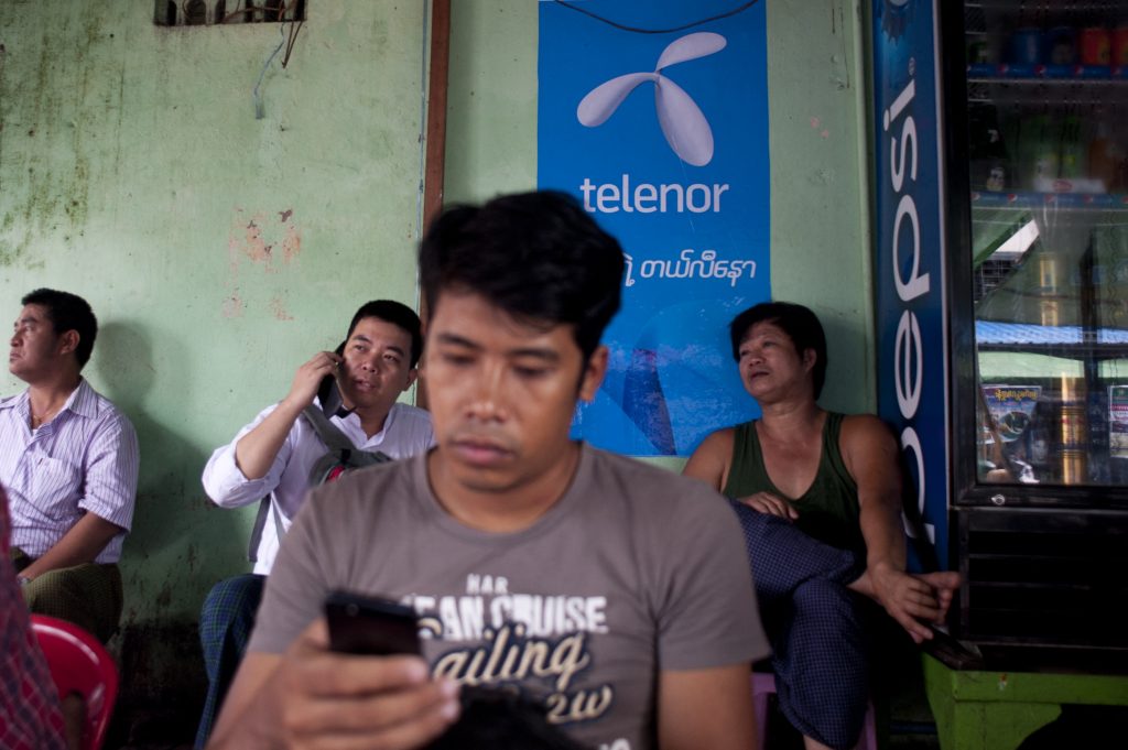 A man uses the internet with a mobile phone in front of a sign advertising Telenor in Yangon on September 26, 2014, shortly after the Norwegian operator launched its network. (AFP)