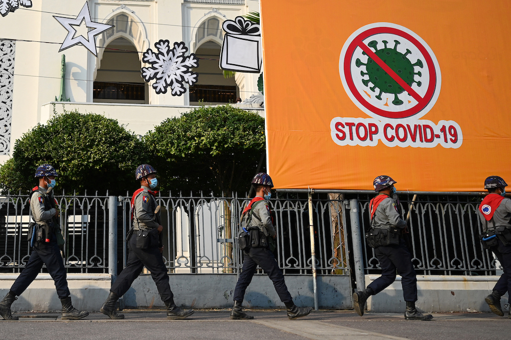 Police march past a COVID-19 prevention banner as protesters gather shortly after the coup in Yangon in February, 2021. (AFP)