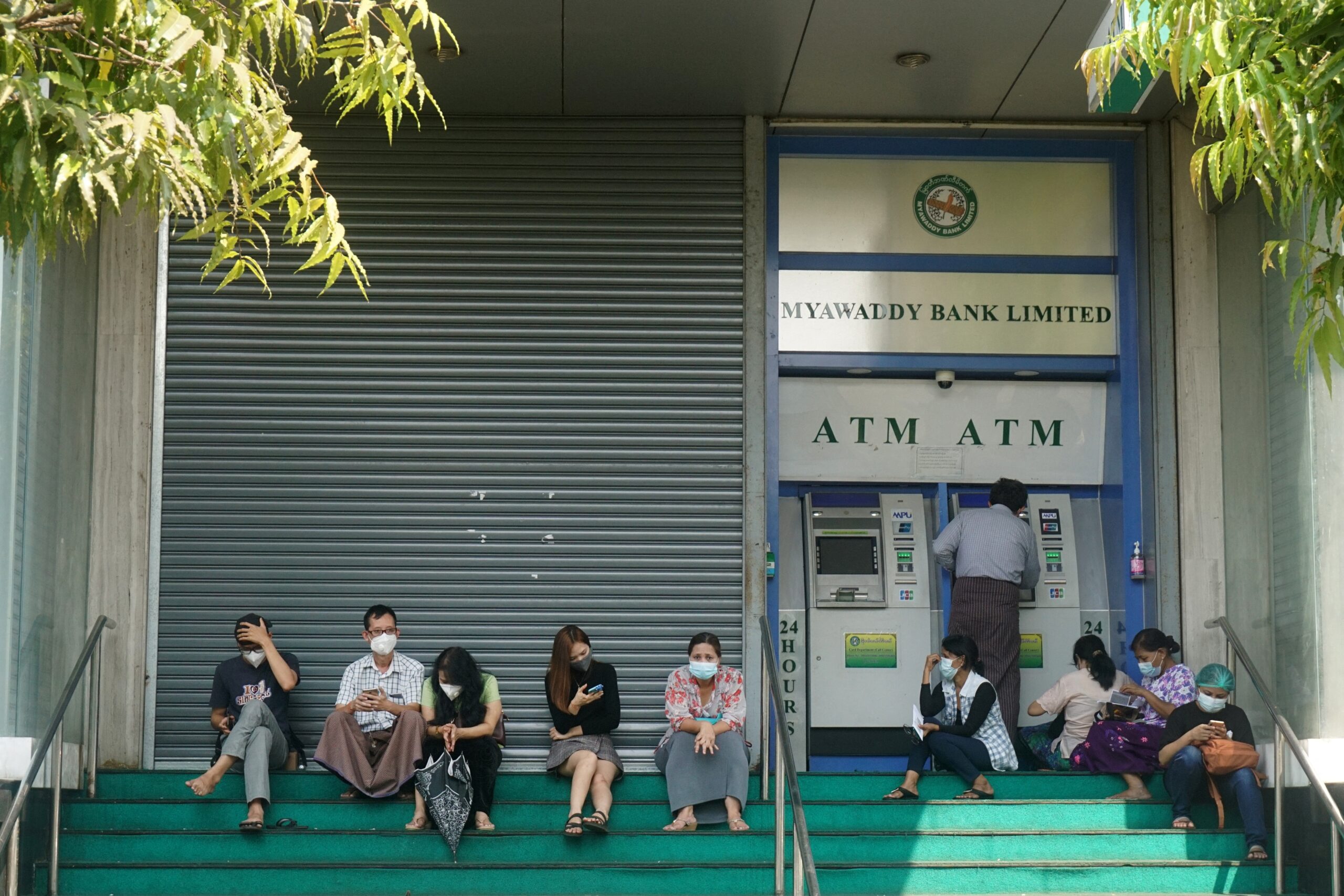 People wait to withdraw money from an ATM outside a closed branch of military-owned Myawaddy Bank in Yangon (Sai Aung Main | AFP)