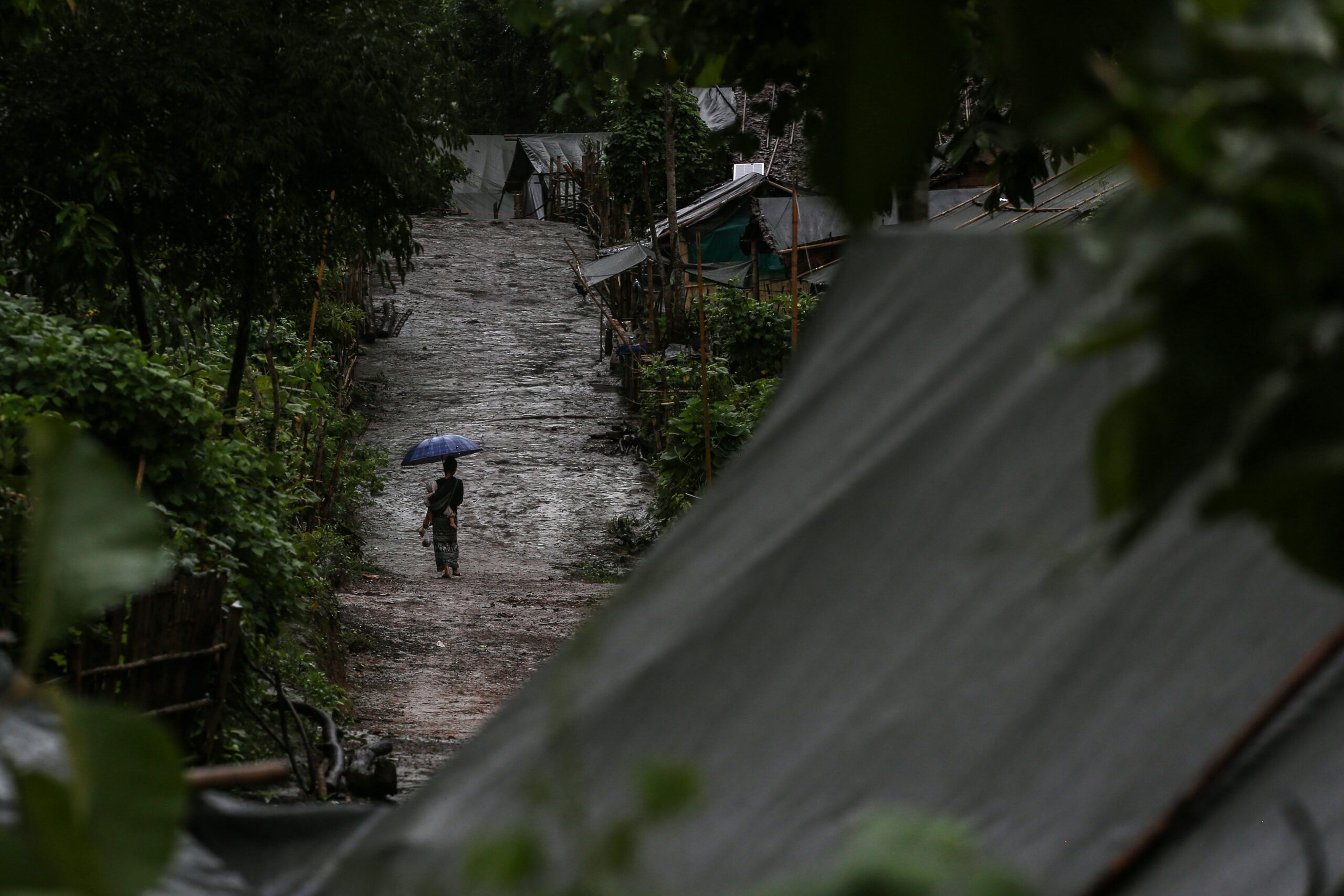 A woman carries her child under heavy rains in an internally displaced people camp in Kayah State in September. (Valeria Mongelli)