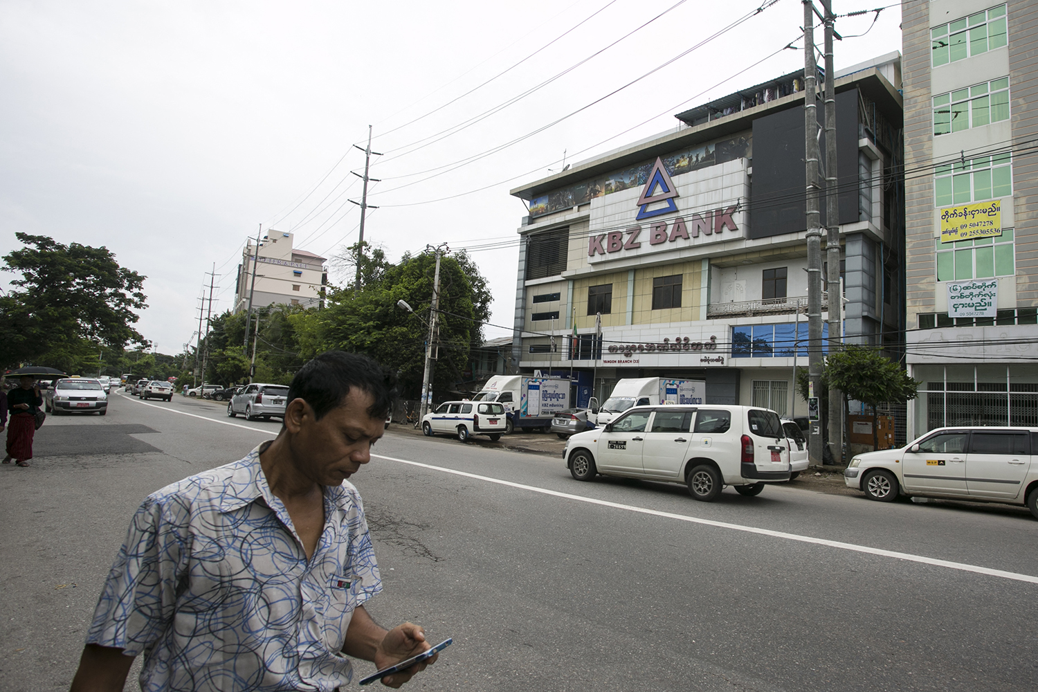 A man looking at his mobile phone walks past a KBZ bank's branch in Yangon on September 6, 2019. (AFP)