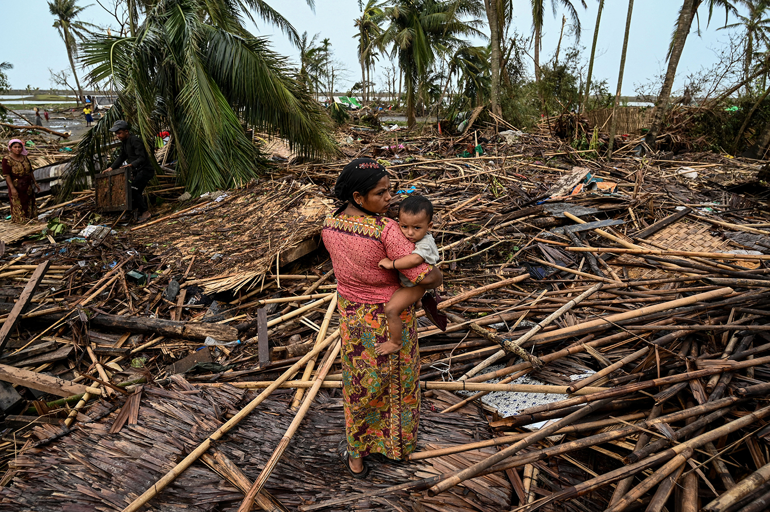 A Rohingya woman carries her baby next to her destroyed house at Basara camp in Rakhine State's Sittwe Township on May 16, after Cyclone Mocha made landfall. (AFP)