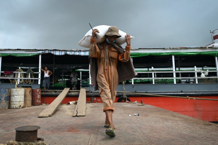 A worker unloads sacks of rice from a boat at the Yangon jetty on July 8. (AFP)