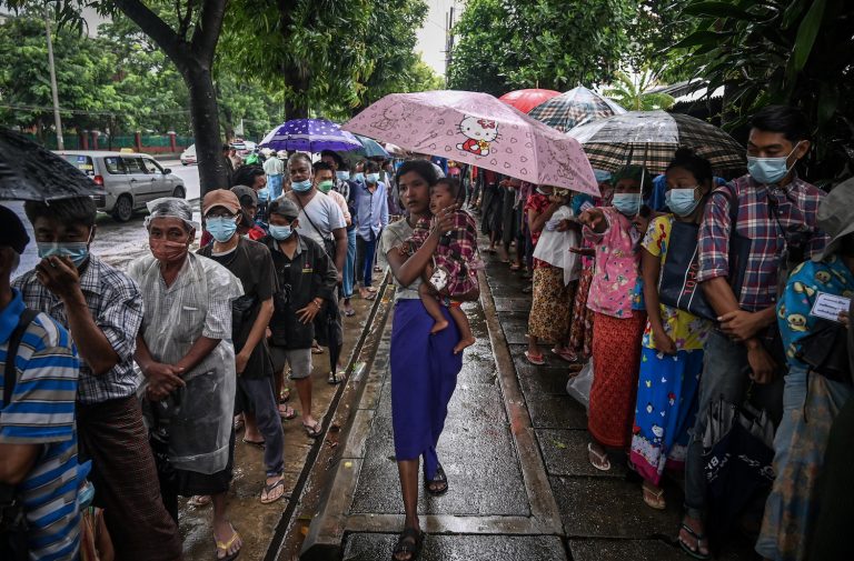 Dozens queue in the rain to receive free meals and by subsidised cooking oil in Yangon as prices for basic commodities soar. (AFP)