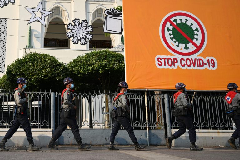 Police march past a billboard related to stopping the spread of COVID-19 as protesters gather for a demonstration against the military coup in Yangon on February 6. (AFP)