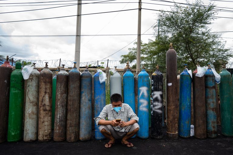 A man using his mobile phone in front of empty oxygen canisters outside a factory in Mandalay on July 31, 2021. (AFP)