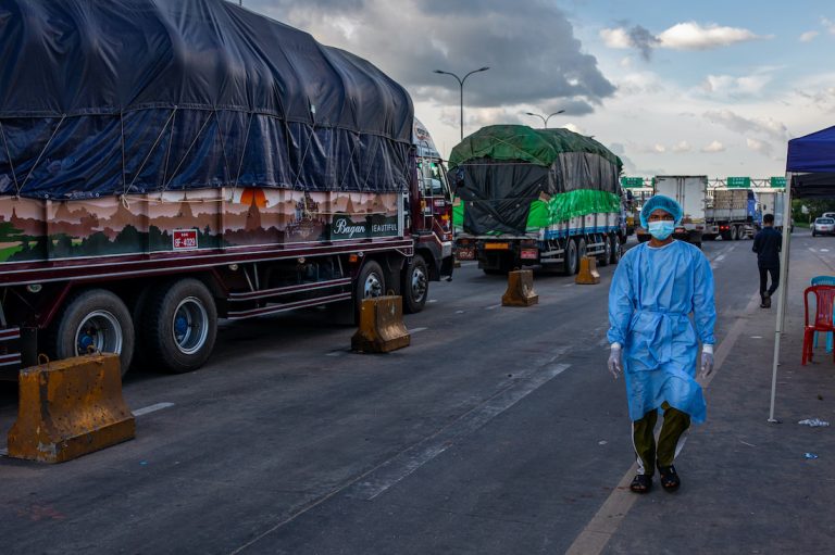 A medical worker walks past trucks lined up at a toll gate along the Yangon-Mandalay Highway, their drivers waiting to be tested for COVID-19. Travel restrictions and COVID-19 transport protocols have caused major disruptions to the country's logistics network. (Hkun Lat | Frontier)