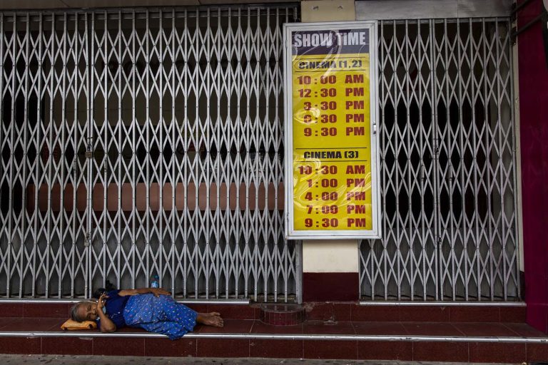 A woman rests in front of the shuttered Shae Saung Cinema on Yangon's Sule Pagoda Road on July 27, 2020. (Hkun Lat I Frontier)