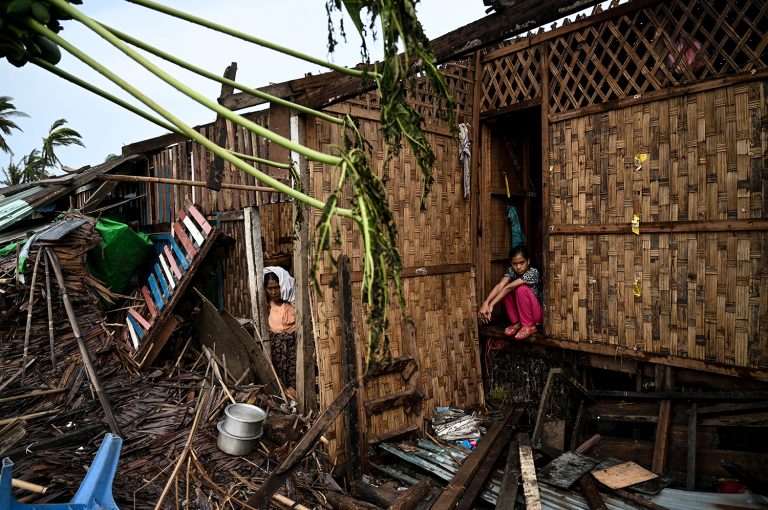 A girl sits outside her damaged house at Basara camp in Sittwe on May 16, 2023. (AFP)