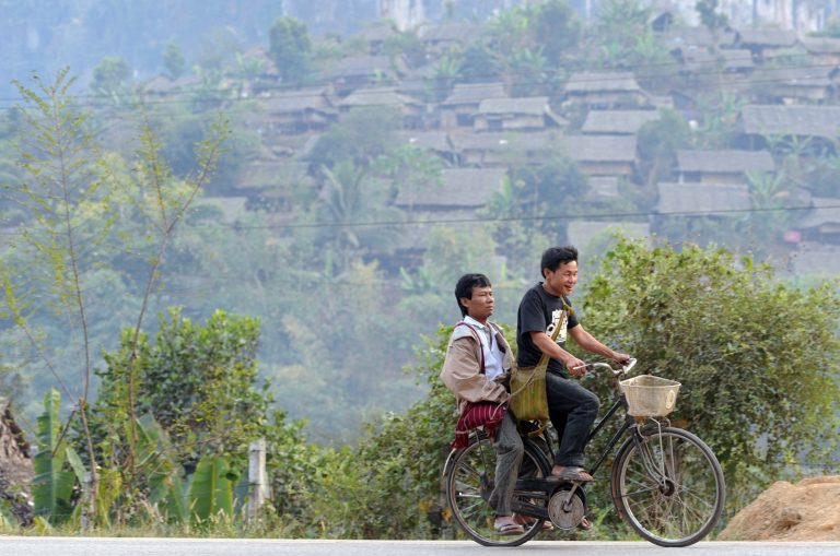 Two Myanmar men ride a bicycle past the Mae La refugee camp in Thailand’s Tak province on January 29, 2012. (AFP)