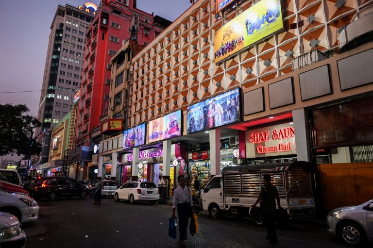 People walk past a cinema in Yangon on March 12, 2020. (AFP)