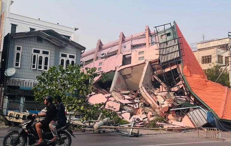 People drive on a motorbike past a collapsed building in Mandalay after an earthquake on March 28. (AFP)