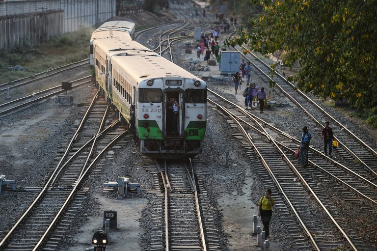 People walk along railway tracks as a train passes in Yangon on March 3, 2020. (AFP)