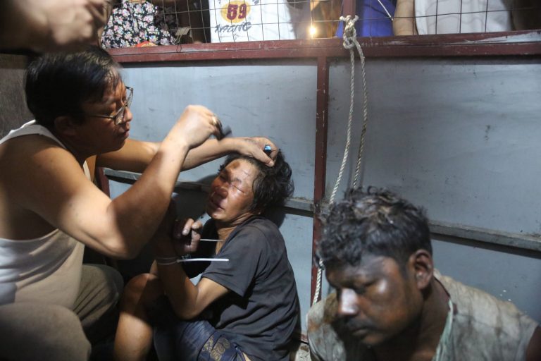 A Yangon resident shaves the eyebrows and head of a man detained by locals in Botahtaung Township after curfew on February 13. Residents suspected the man and two others caught the same night had been sent to cause mayhem in the neighbourhood but there was little evidence to support this allegation. (Frontier)